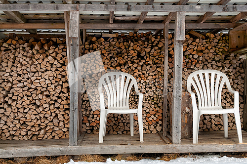 Image of Wooden storage structure with stacked firewood and two white cha