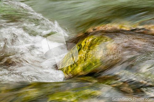 Image of Water flows over moss-covered rocks in a serene river during a b