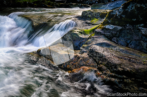 Image of Gentle water flows over smooth rocks in a serene riverscape capt