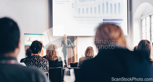 Image of Speaker giving a talk in conference hall at business event. Rear view of unrecognizable people in audience at the conference hall. Business and entrepreneurship concept.