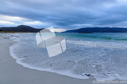 Image of Waves gently lap against the shore of a serene beach under a clo