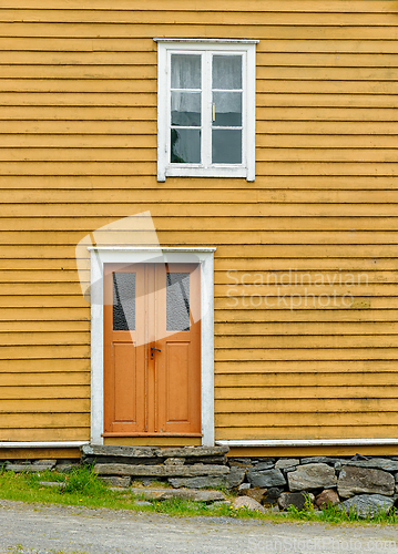 Image of Yellow wooden house with orange door and window in a rural setti
