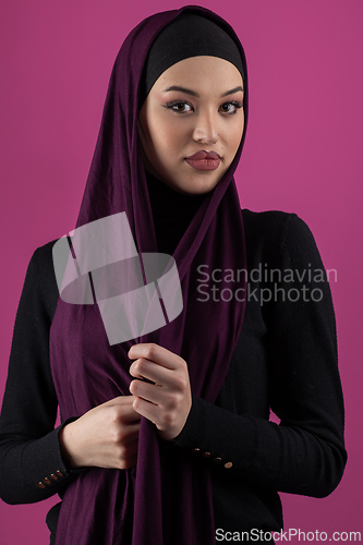 Image of Beautiful Muslim woman in a hijab posing elegantly in a studio with a pink background.