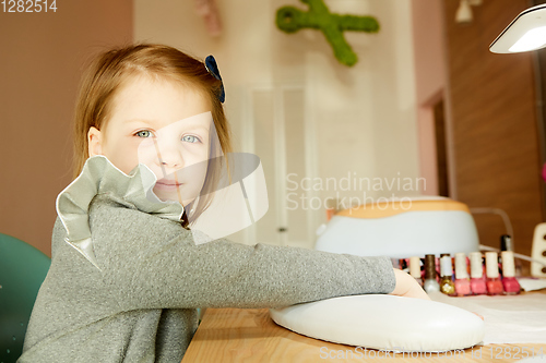 Image of Little girl in nail salon receiving manicure by beautician. Little girl getting manicure at beauty salon.