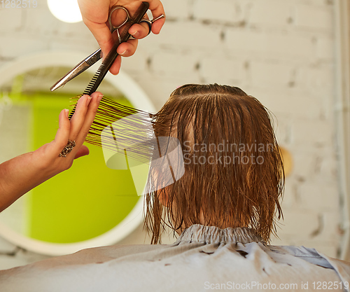 Image of Hairdresser making a hair style to cute little girl.