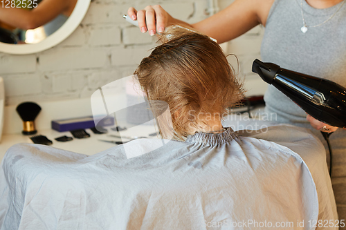 Image of Hairdresser making a hair style to cute little girl.