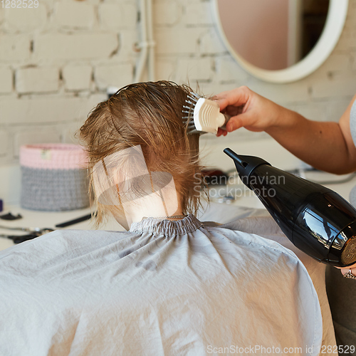 Image of Hairdresser making a hair style to cute little girl.