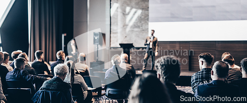 Image of Speaker giving a talk in conference hall at business event. Rear view of unrecognizable people in audience at the conference hall. Business and entrepreneurship concept.