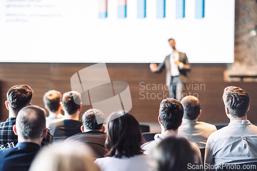 Image of Speaker giving a talk in conference hall at business event. Rear view of unrecognizable people in audience at the conference hall. Business and entrepreneurship concept.