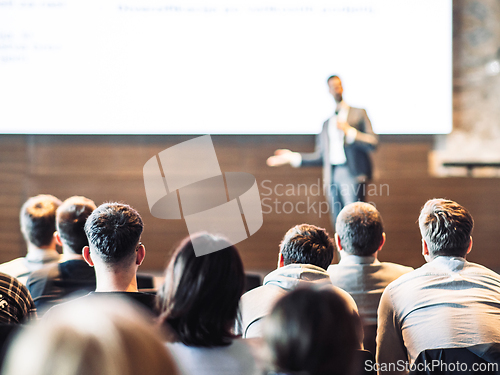 Image of Speaker giving a talk in conference hall at business event. Rear view of unrecognizable people in audience at the conference hall. Business and entrepreneurship concept.