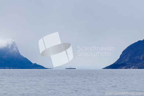Image of Foggy landscape with ferry crossing serene water between snow-ca