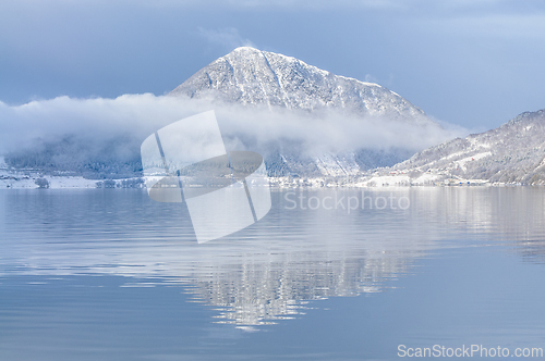 Image of Serene winter landscape with snow-covered mountain and calm lake
