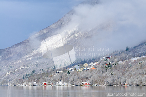 Image of Snow-covered mountains reflect in a serene lake with vibrant hou