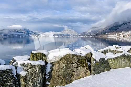 Image of Snow-covered rocks by still water reflect the beauty of winter i