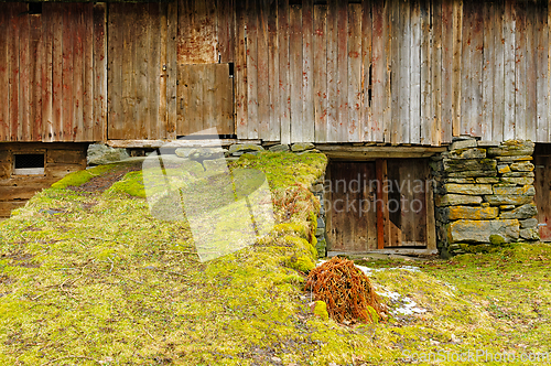 Image of Rustic wooden structure with stone foundation and grassy slope i