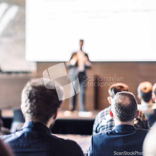 Image of Speaker giving a talk in conference hall at business event. Rear view of unrecognizable people in audience at the conference hall. Business and entrepreneurship concept.