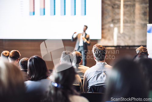 Image of Speaker giving a talk in conference hall at business event. Rear view of unrecognizable people in audience at the conference hall. Business and entrepreneurship concept.