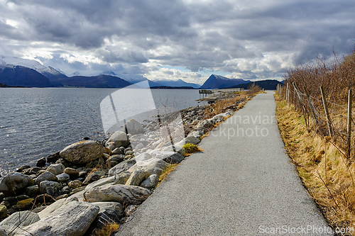 Image of Scenic seaside pathway surrounded by mountains and cloudy skies 