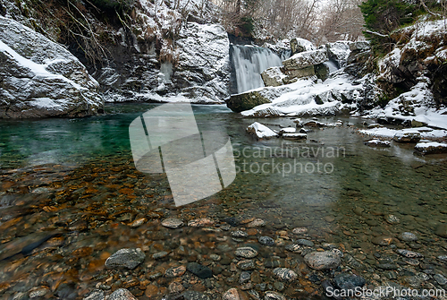 Image of Serene winter waterfall surrounded by snow-covered rocks and cle