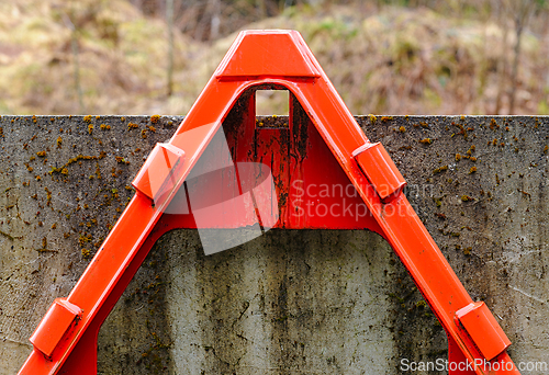 Image of Bright red triangular barrier stands against a weathered concret