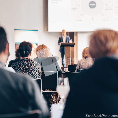 Image of Speaker giving a talk in conference hall at business event. Rear view of unrecognizable people in audience at the conference hall. Business and entrepreneurship concept.