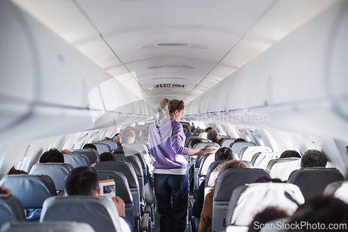 Image of Interior of airplane with passengers on seats and female traveler walking the aisle. Commercial economy flight service concept.