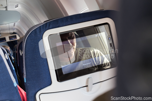 Image of Reflection of a passenger on an airplane touch screen monitor while watching cartoon during long flight. Entertainment service system in aircraft.