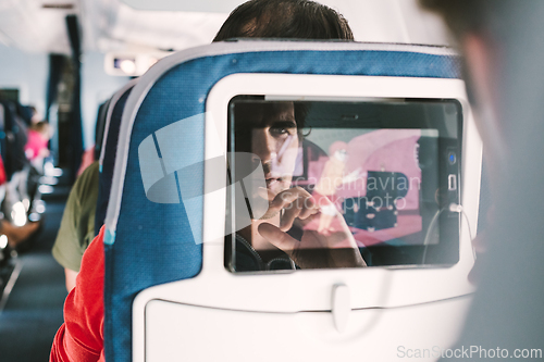 Image of Reflection of a passenger on an airplane touch screen monitor while watching cartoon during long flight. Entertainment service system in aircraft.
