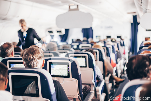Image of Interior of airplane with passengers on seats and stewardess in uniform walking the aisle, serving people. Commercial economy flight service concept.