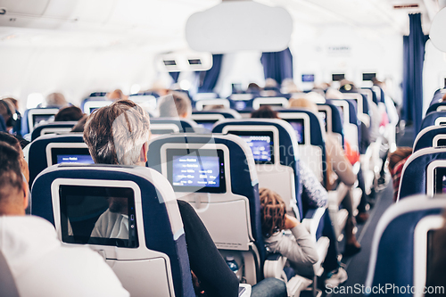 Image of Interior of airplane with passengers on seats and stewardess in uniform walking the aisle, serving people. Commercial economy flight service concept.