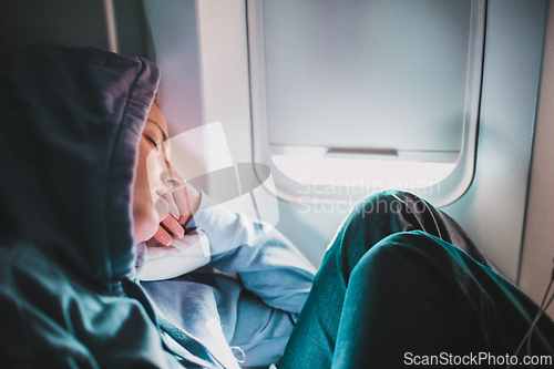Image of Tired blonde casual caucasian woman wearing sporty hoodie napping on seat while traveling by airplane. Commercial transportation by planes. Authentic image of real people.