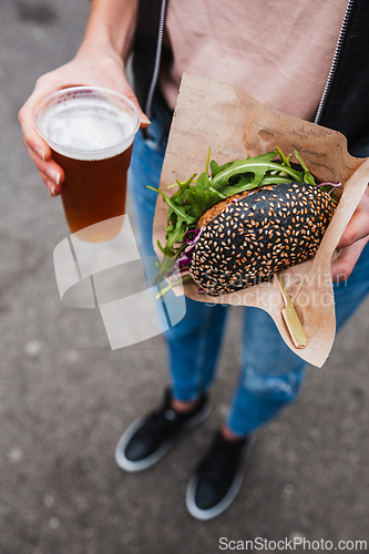 Image of Close up of woman hands holding delicious organic salmon vegetarian burger and homebrewed IPA beer on open air beer an burger urban street food festival in Ljubljana, Slovenia.