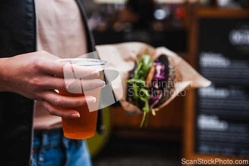 Image of Close up of woman hands holding delicious organic salmon vegetarian burger and homebrewed IPA beer on open air beer an burger urban street food festival in Ljubljana, Slovenia.