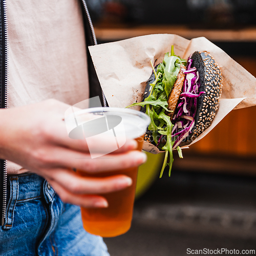 Image of Close up of woman hands holding delicious organic salmon vegetarian burger and homebrewed IPA beer on open air beer an burger urban street food festival in Ljubljana, Slovenia.