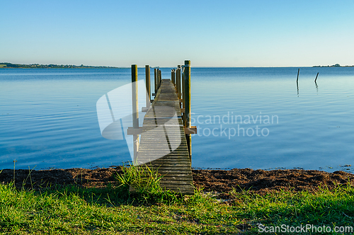 Image of Dock extending into calm lake at sunset with clear blue sky and 