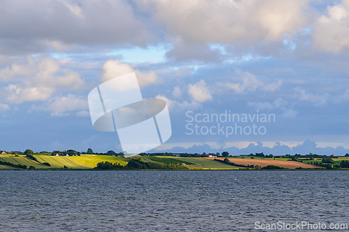 Image of Scenic landscape view of fields and clouds over a serene body of