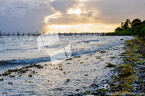 Image of Sunset over a tranquil beach with gentle waves and seaweed along