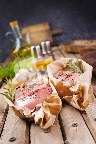 Image of Fresh chicken breast fillet on a wooden cutting board with spices, dark rustic background.