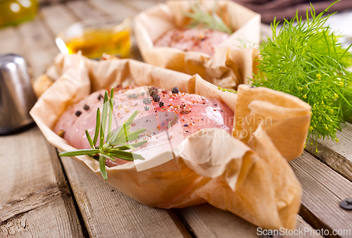 Image of Fresh chicken breast fillet on a wooden cutting board with spices, dark rustic background.