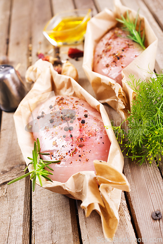 Image of Fresh chicken breast fillet on a wooden cutting board with spices, dark rustic background.