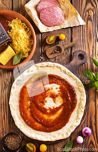 Image of Raw pizza dough with tomato sauce and basil leaves.