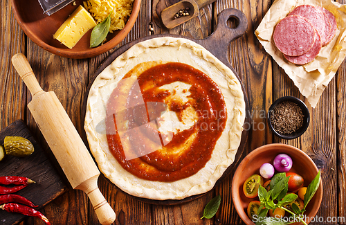 Image of Raw pizza dough with tomato sauce and basil leaves.