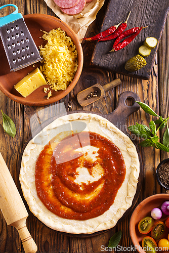 Image of Raw pizza dough with tomato sauce and basil leaves.