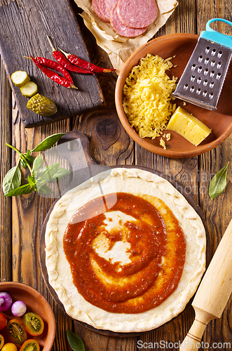 Image of Raw pizza dough with tomato sauce and basil leaves.
