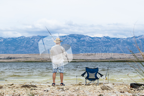 Image of Rear view of old unrecognizable fisherman wearing a straw hat, holding a fishing pole.