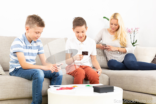 Image of Brothers playing card game on living room sofa at home supevised by their mother.