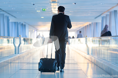 Image of Businessman walking and wheeling a trolley suitcase at the lobby, talking on a mobile phone. Business travel concept.