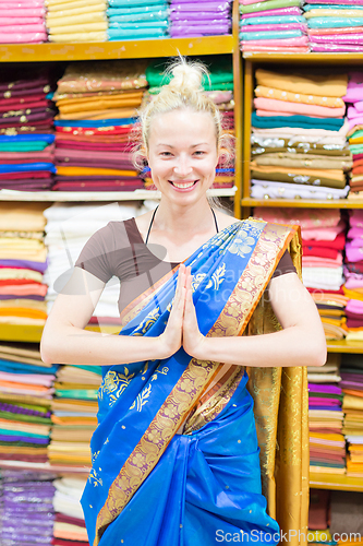 Image of Travel photo of beautiful blond Caucasian tourist woman trying to wear a traditional Indian saree in local saree shop as part of authentic travel experience.