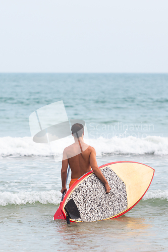 Image of Rear view of unrecognizable male surfer at tropical beach with sup surf board and paddle in his hands