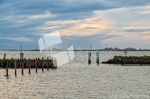 Image of Sunset over calm waters with wooden pier and distant shoreline i